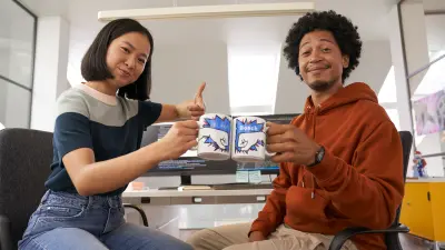 Mann und Frau am Arbeitsplatz, stoßen mit Kaffeetassen an