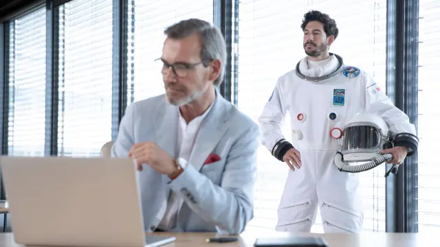 Mann am Laptop und Astronaut dahinter stehend