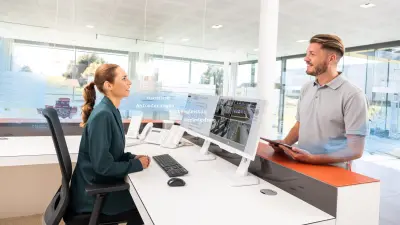 Frau sitzt am Empfangsschalter mit Bildschirmen vor sich, während sie einen Mann bedient