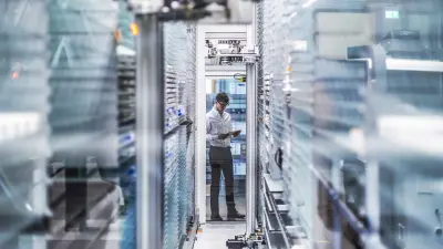 Man in white shirt standing with tablet between server racks in modern data center.