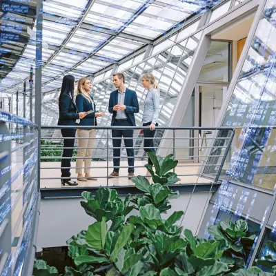 Gruppe von Kolleginnen und Kollegen in einem Bürogebäude mit großen Glasflächen, digitale Screens 