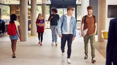 Mehrere Studenten laufen sich unterhaltend durch einen Gang in einer Universität