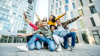 Mehrere Studenten auf einem Hochschulgelände lachen und bilden mit ihren Armen einen Stern