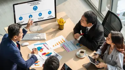 Vier Personen am Tisch in Besprechung, auf dem Monitor eine Präsentation