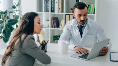 Ein Arzt und eine Verwaltungsmitarbeiterin schauen gemeinsam in einen Laptop