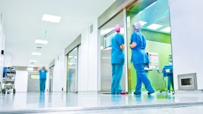Zwei Krankenhausmitarbeiter in OP-Kleidung verlassen einen Operationssaal