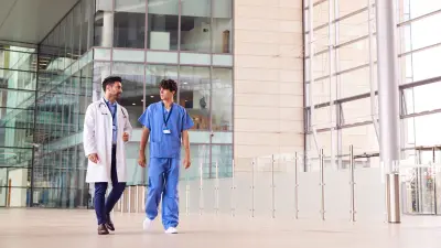 Ein Arzt und ein Krankenpfleger gehen auf einem großen Gang eines Klinik-Campus