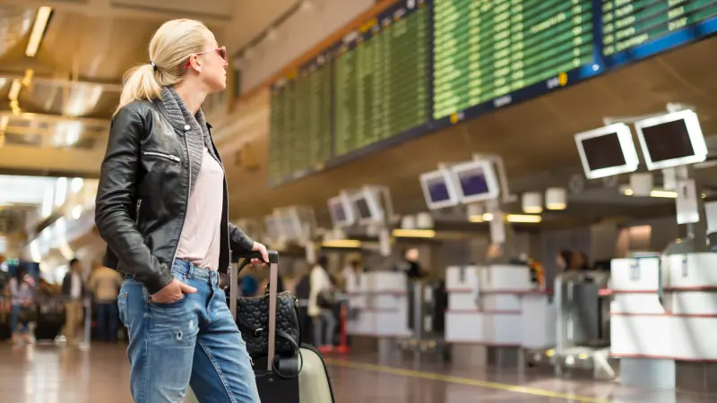 Lässige blonde Frau sucht in der Abflughalle des Flughafens auf der Anzeigetafel nach ihrem Flug