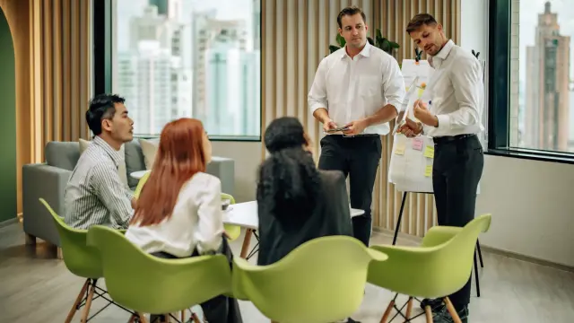 Zwei Berater präsentieren einem Team in einem Besprechungsraum ein Konzept auf einem Flipchart. 