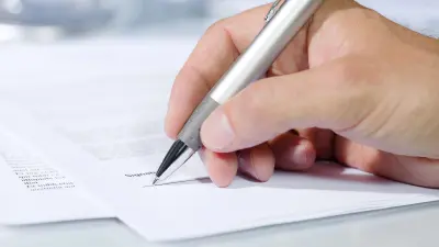 Hand unterschreibt ein Dokument mit einem Stift – Symbol für Antragstellung. 