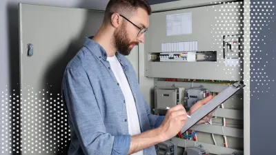 Mann steht vor einem geöffneten Schaltschrank und macht sich Notizen auf seinem Klemmbrett