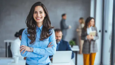 Lächelnde Frau steht in einem Büro. Perfekte Umgebungsbedingungen in Räumen sorgen für zufriedene Mitarbeiterinnen und Mitarbeiter