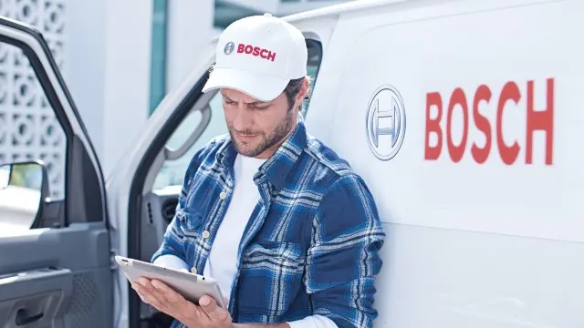 Bosch Techniker vor seinem Auto mit Tablet in der Hand