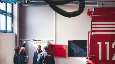 Halle der Feuerwache mit drei Personen und installierter Brandmeldekamera 