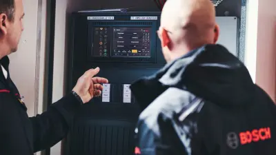 Zwei Personen stehen vor installierter Brandmelderzentrale
