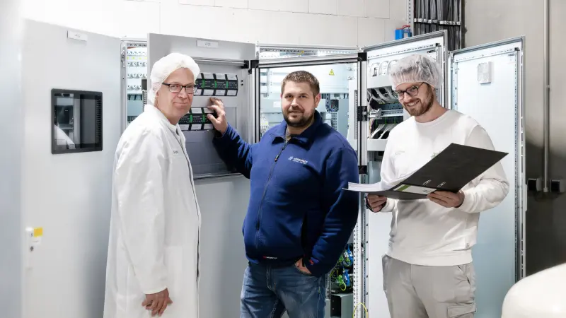 Martin Hartmann and two employees of Allgäu Käse eG in front of the control cabinet