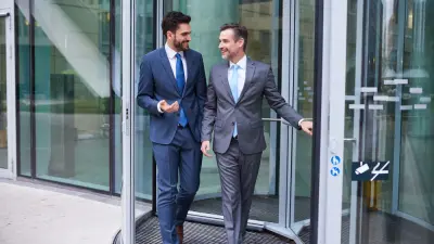 Zwei Business-Männer gehen durch die Drehtür aus einem Bankfoyer nach draußen