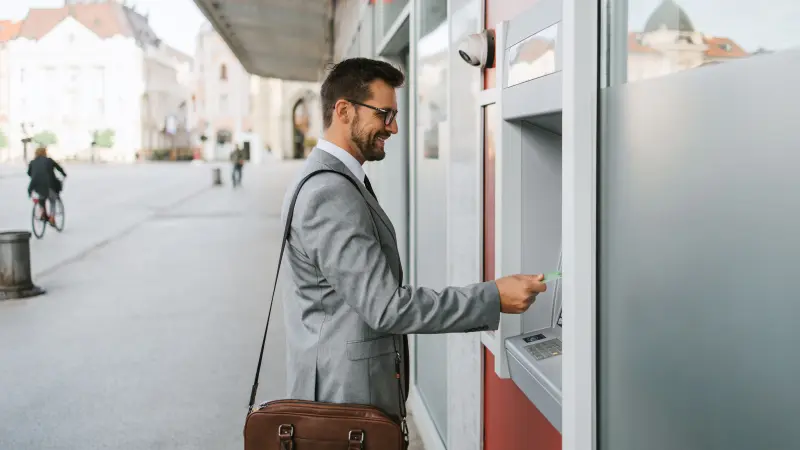 Sicherheit im Bankfoyer: Mann steht mit Smartphone in der Hand vor einem Geldautomaten