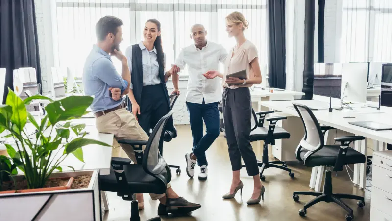 Vier Kollegen:innen unterhalten sich stehend in einem Büro, eine davon hat ein Tablet in der Hand