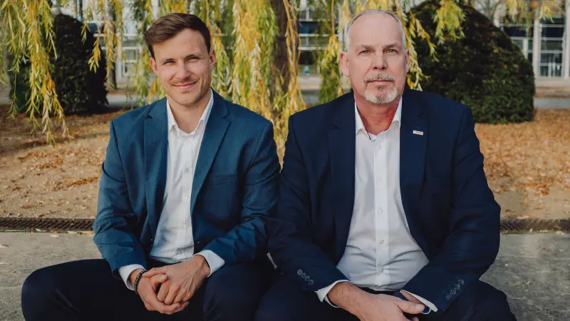 Felix Weidinger und Jens Jürgensen sitzen nebeneinander und blicken in die Kamera