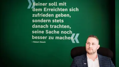 Marius Kaiser sits in the Service & Supply Chain Campus building in Stuttgart-Feuerbach in front of a wall with a quote from Robert Bosch