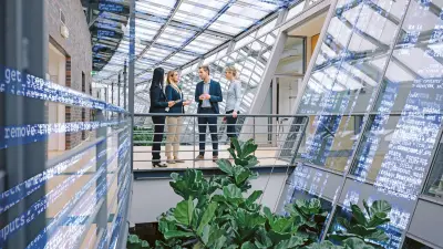 Group of colleagues in an office building with large glass surfaces, digital screens
