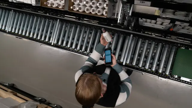 Kamera von oben dokumentiert Mitarbeiterin, die Haarkosmetik über einem Rollband scannt