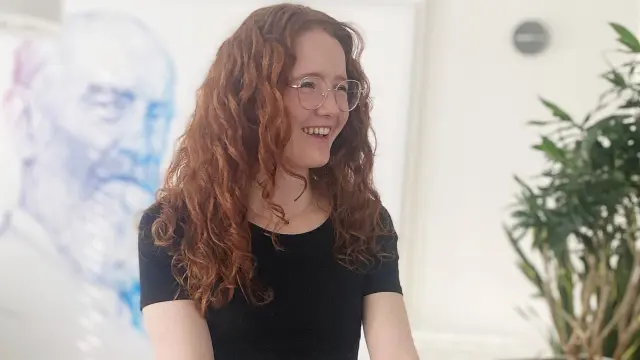 Romina steht lachend an einem Stehtisch mit ihrem Laptop, im Hintergrund ein Bild von Robert Bosch