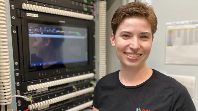 Romina steht lachend an einem Stehtisch mit ihrem Laptop, im Hintergrund ein Bild von Robert Bosch