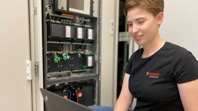 Sabine notiert die Ergebnisse in ihrem Laptop, dabei sitzt sie vor dem Schaltschrank beim Kunden