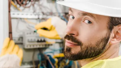 Two male safety managers dressed with safety vests and helmets stand before a white board and lecture to a class. One man holds a fire extinguisher