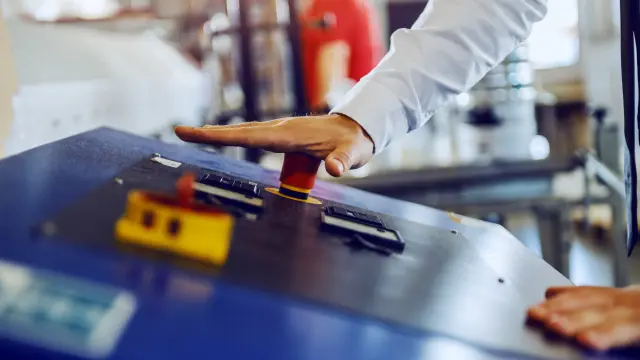 Male hand on a machine ready to press the big red Stop button