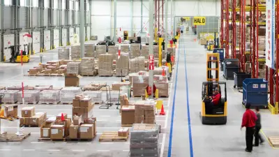 inside of a warehouse is shown. Many boxes, people and forklifts.