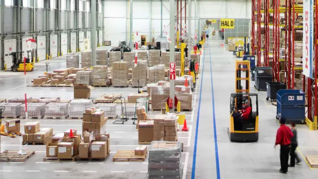 inside of a warehouse is shown. Many boxes, people and forklifts.