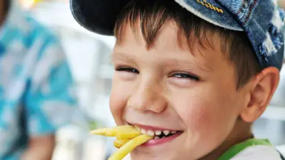 Little boy with a baseball cap happily munching french fries