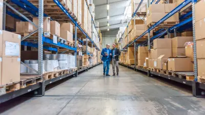 Two men walking between storage shelves packed with goods