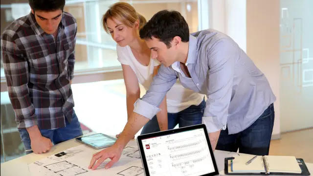 Planners study building plans on a table with a laptop