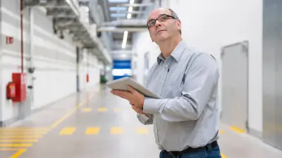 Man with Ipad looking at detectectors installed on the ceilling and doing maintenance